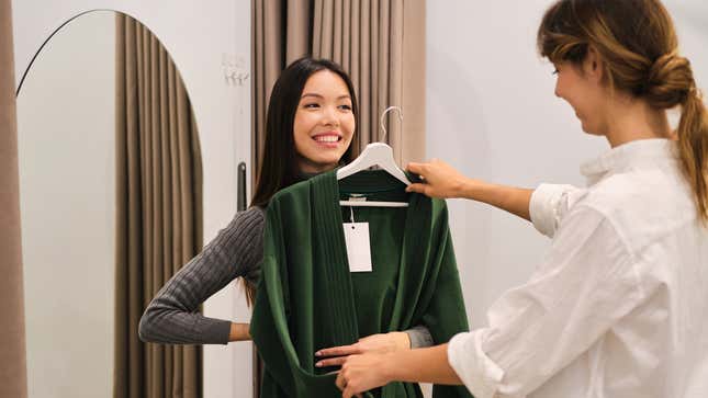 A woman holds a green velvet robe on a hanger up to another women.