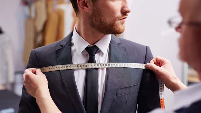 A person wearing a suit is measured by a tailor.